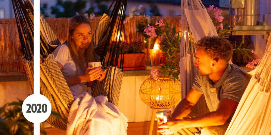 Eine junge Frau und ein junger Mann sitzen im dunkeln bei Kerzenlicht in Hängesesseln. Die Frau hat eine Decke und eine Tasse in den Händen